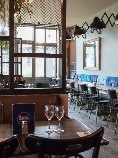 Intérieur de la rôtisserie Maison Becquey de Paris, banquette avec assises en cuir, dossiers nuancés de bleu et luminaires croisillons. Décoration par le Studio Emma Roux