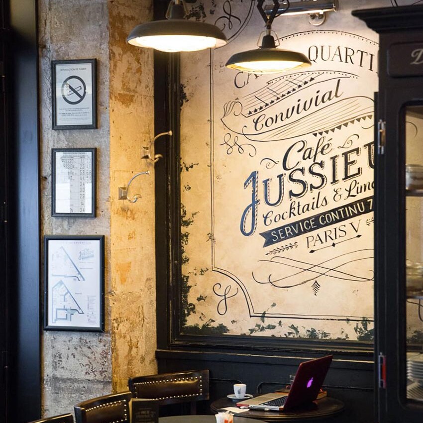 Intérieur du Café Jussieu de Paris avec son panneau décor, ses suspensions croisillon et ses assises en cuir.