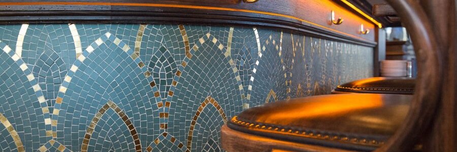 Comptoir en bois et mosaique de la brasserie Le Manfred à Paris avec ses chaises en bois et assises en cuir. Décoration par le Studio Emma Roux