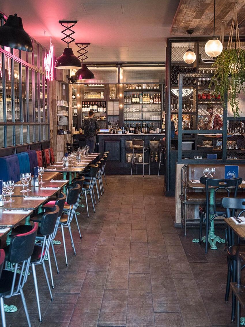 Intérieur de la rôtisserie Maison Becquey de Paris, banquette avec assises en cuir, dossiers nuancés de bleu, néon rose, parquet et luminaires croisillons. Décoration par le Studio Emma Roux
