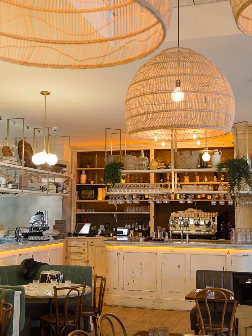 Intérieur du restant Simonetta de Paris avec des luminaires naturels en suspension. On aperçoit au fond le comptoir en bois blanc vieilli. Décoration par le Studio Emma Roux