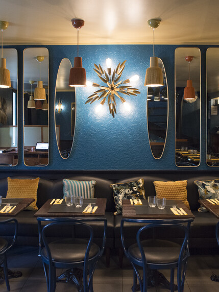 Restaurant Chez Plumeau à Montmartre - Décoration Studio Emma Roux. Jeux de miroir, appliques vintage en laiton, coussins à motifs, suspensions à frange.